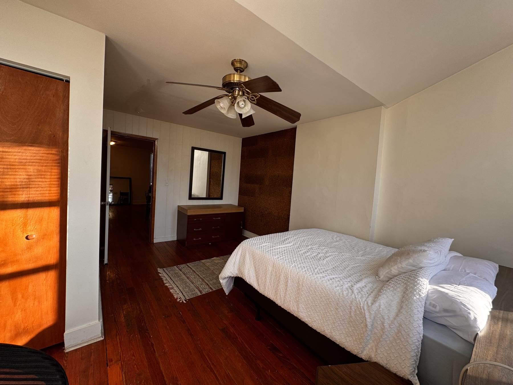 The Geneva room at Edelweiss: a made bed against a paneled wall beside a tall wooden wardrobe, with a mirror and a chest of drawers on dark wood floors.