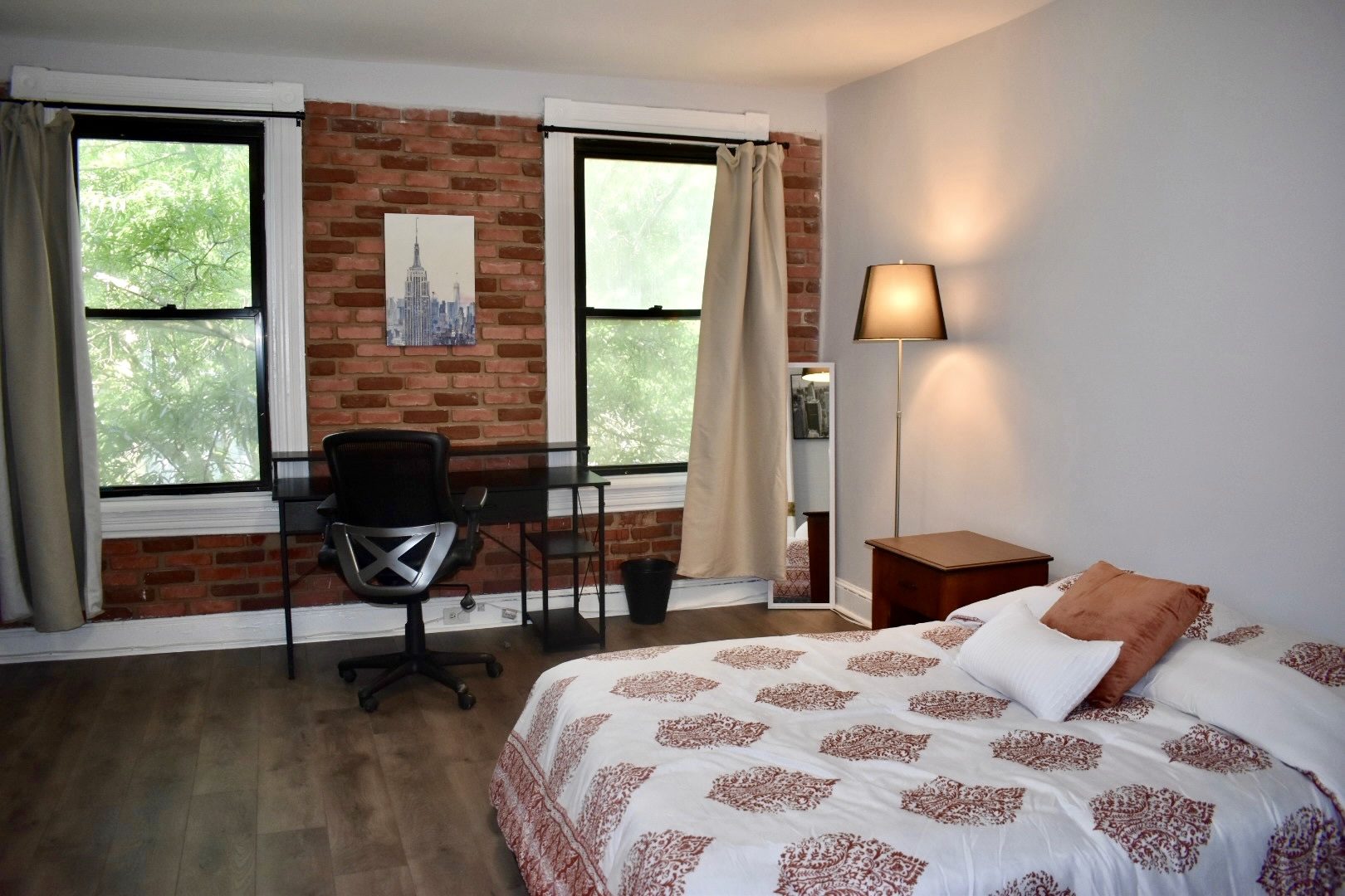 Room 301 at Gotham: a bed with a patterned cover against an exposed brick wall, a desk and chair under the window and a lamp on the side table.