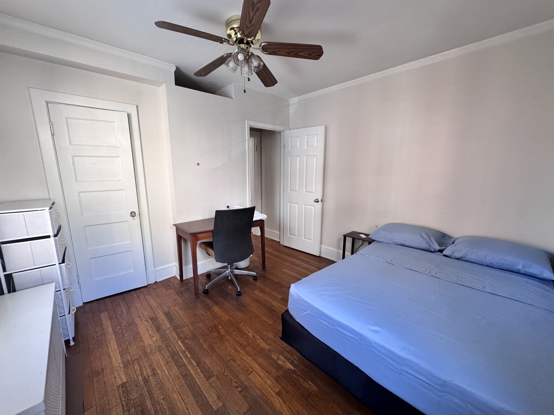 Room 101 at Lincoln A: a bed made up in blue on dark wood floors, with a desk and chair between two doors and a chest of drawers alongside.