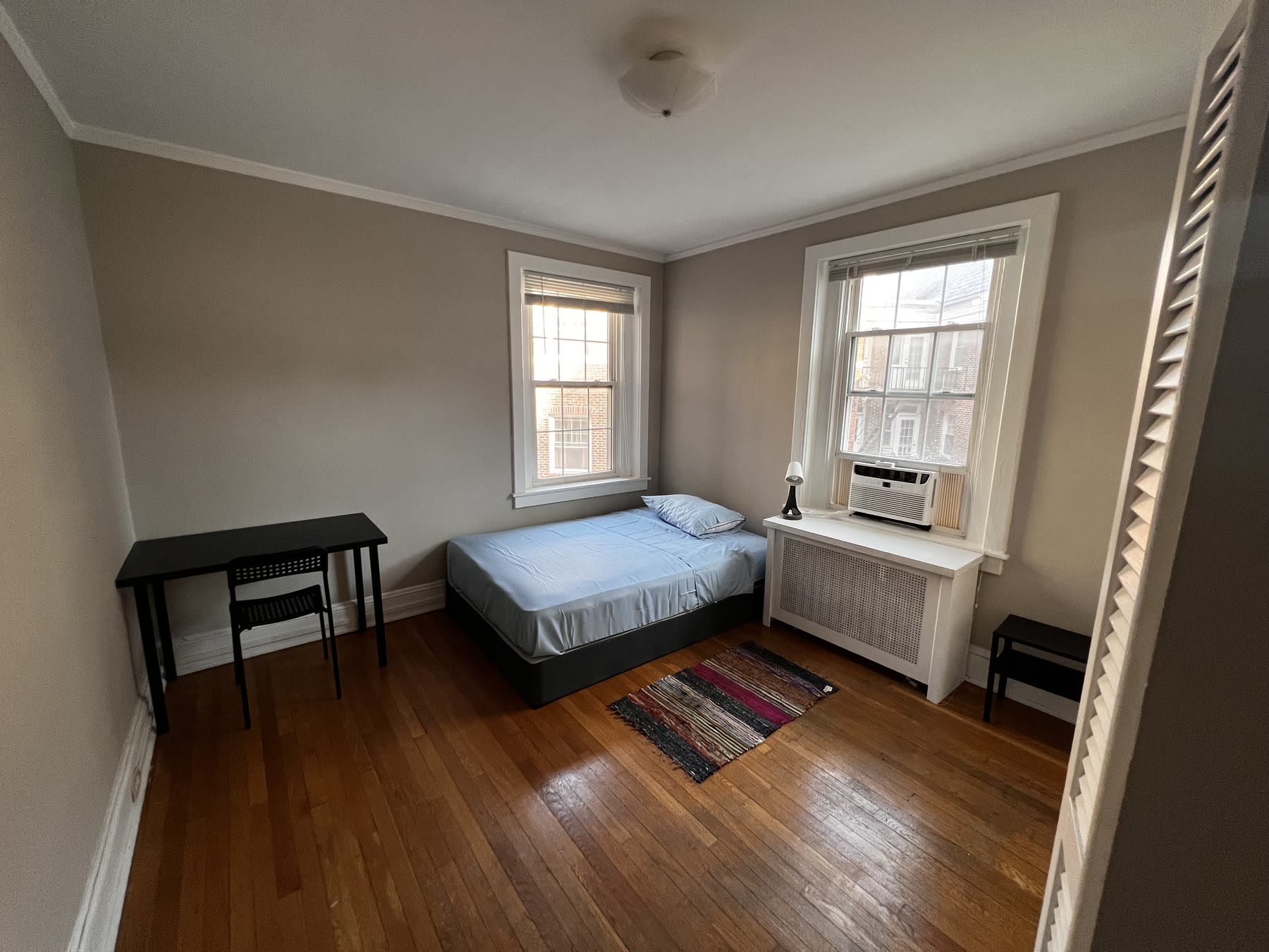 Room 103 at Lincoln C: a single bed between two sash windows, with a desk against the wall and a runner rug on the wood floor.