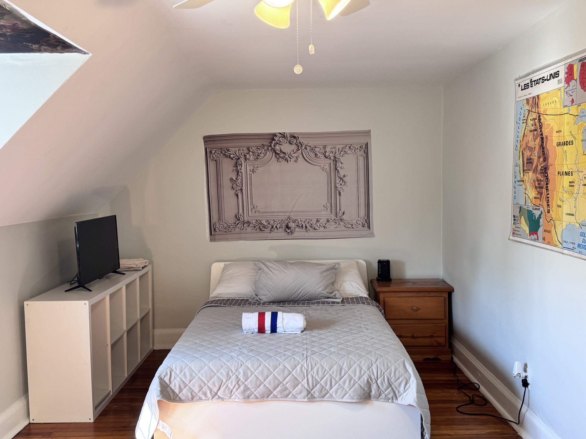 The Saint-Germain room at Lutetia: a bed beneath a carved plaster panel, with a television on a low white unit and a framed Paris map beside the window.