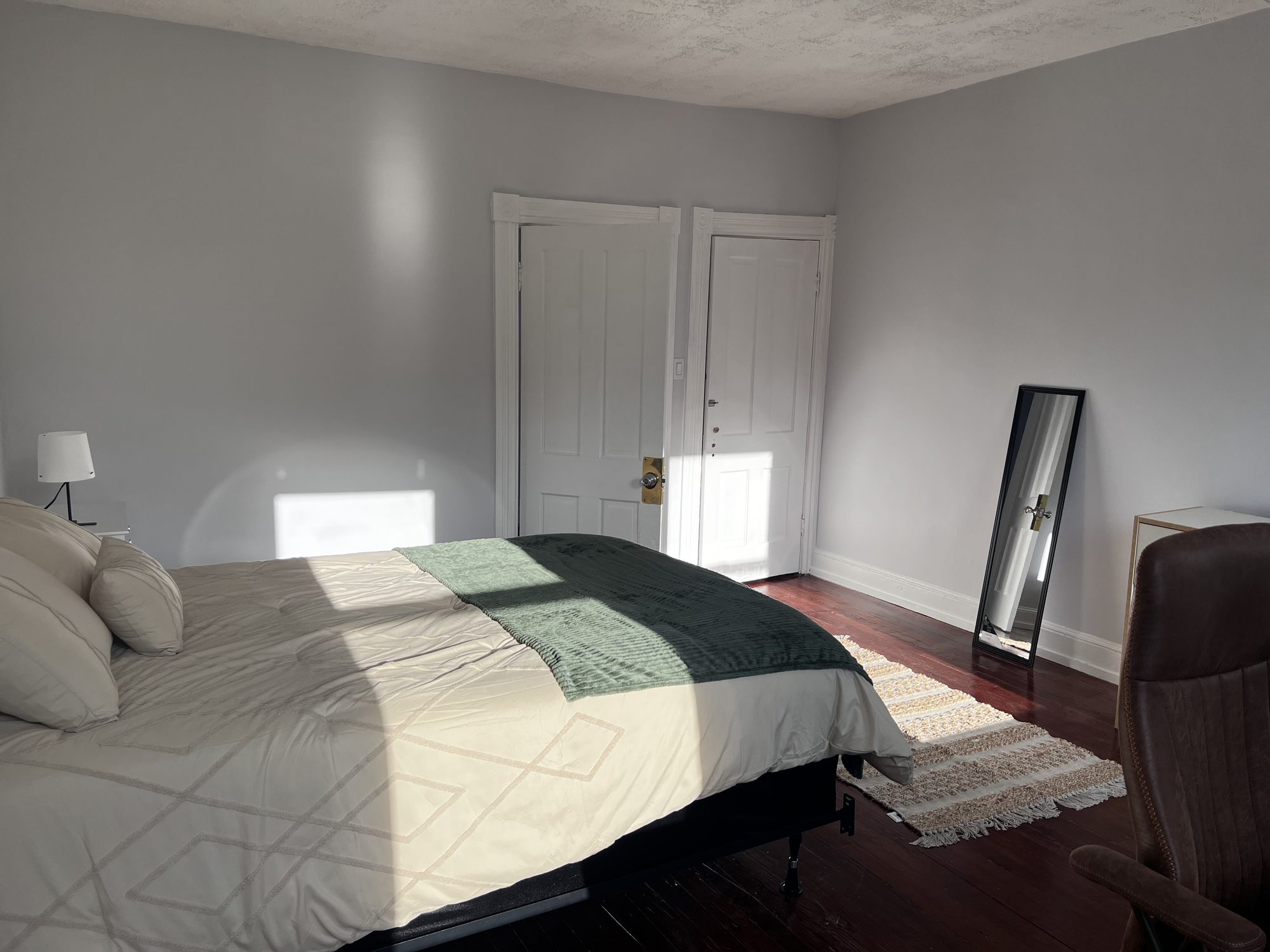 Room 301 at Na'Yo: a wide bed with a green and white cover on dark wood floors, a tall mirror against the wall and light coming through the door.