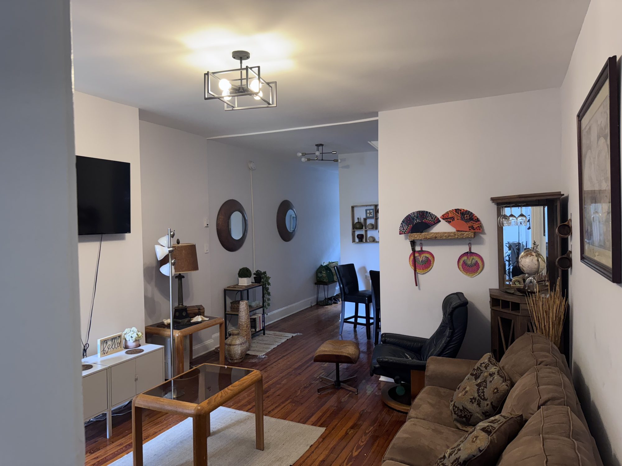 Na'Yo's living room: a corner sofa and low table, with carved masks, round mirrors and framed pictures grouped on the wall above.
