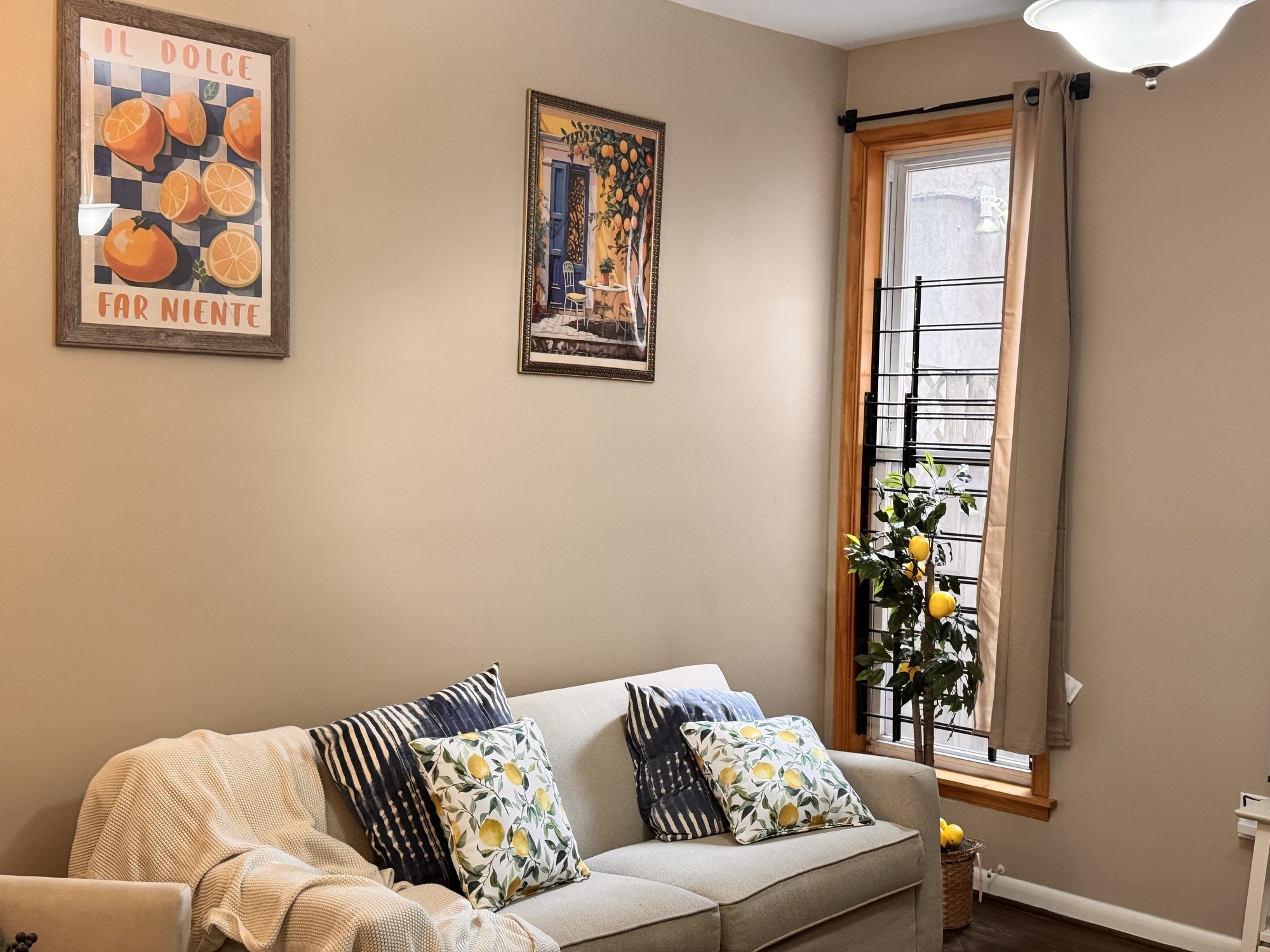 Siena's living room: a cream sofa with patterned cushions beside a tall curtained window, under framed Italian posters.