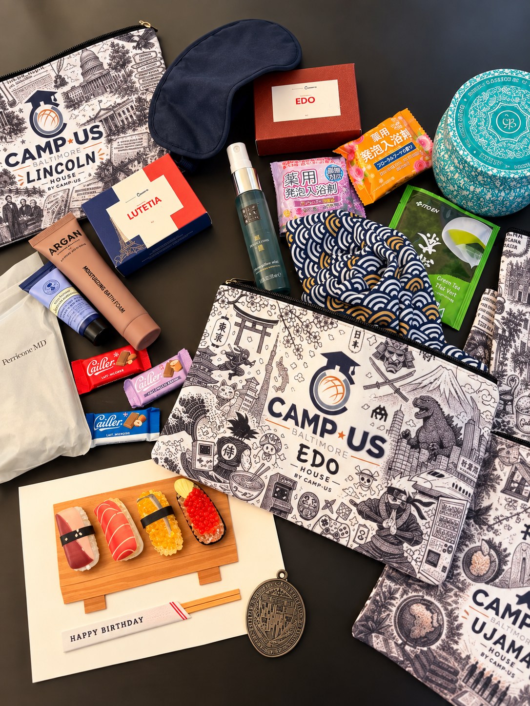 A CAMP-US welcome package laid out: branded Lincoln, Edo and Ujamaa house pouches with toiletries, Japanese bath salts, green tea, chocolates and a card